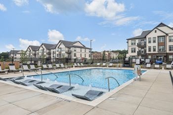 A swimming pool with lounge chairs in front of an apartment building